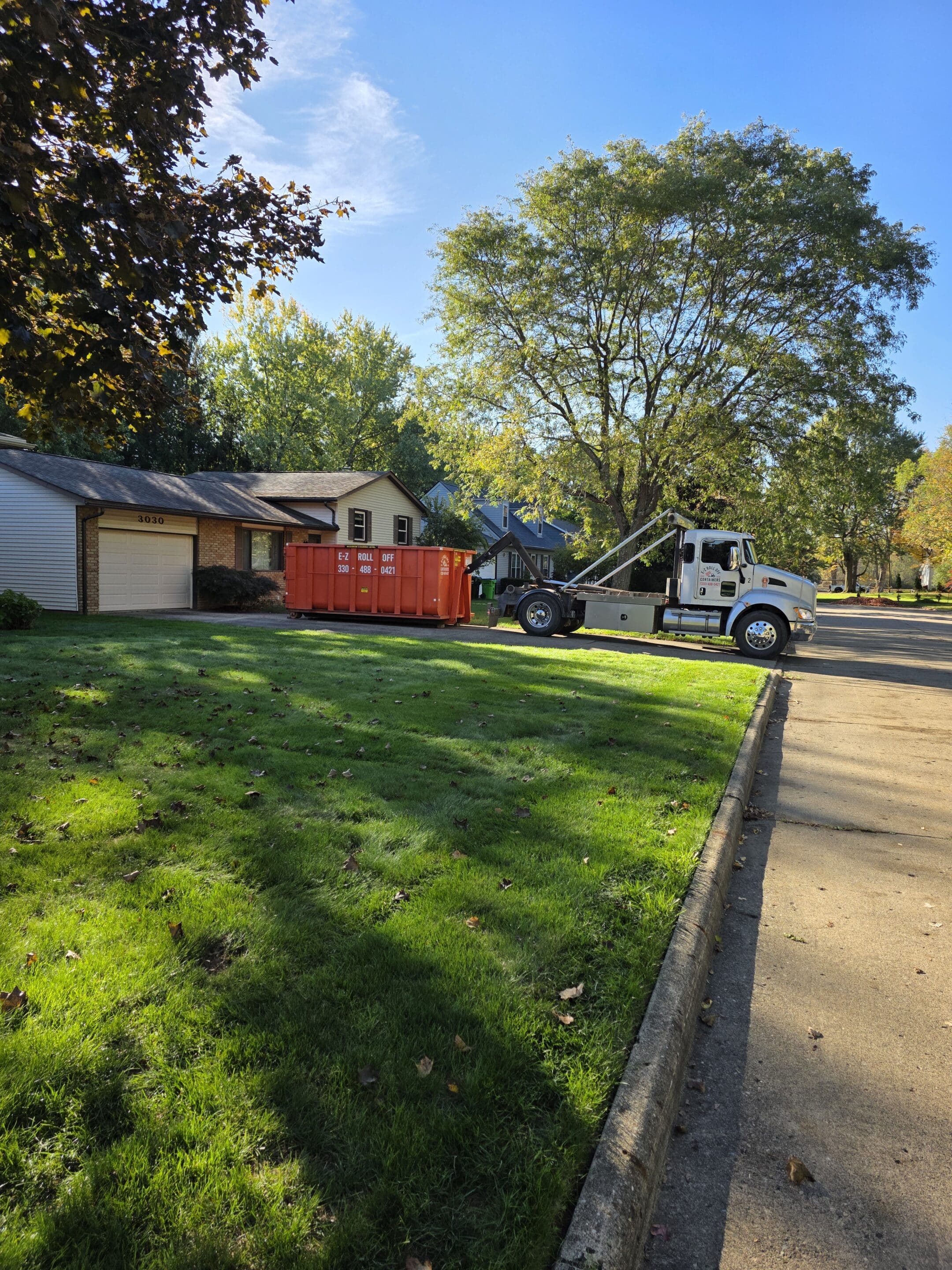 Roll-off dumpster being delivered to a residential driveway in an Alliance, Ohio neighborhood by a white E-Z Roll Off truck.